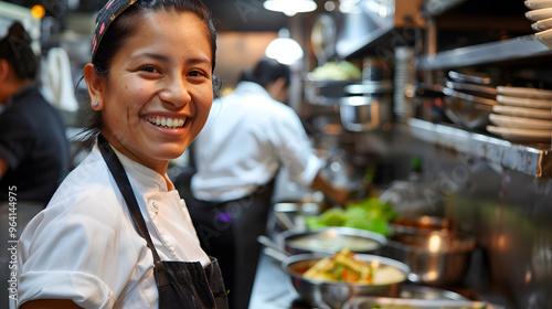 A joyful female chef grins broadly while preparing food in a bustling restaurant kitchen 