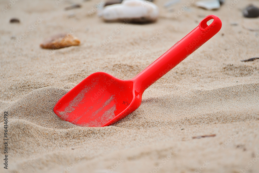 children's red shovel in yellow sand on the beach children's red shovel in yellow sand on the beach