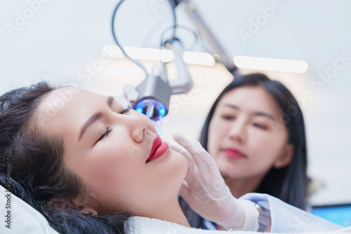 Side view of asian woman getting resurfacing laser fraxel dual and ultrasound face treatment in medical spa center. skin rejuvenation concept	 photo