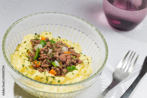 Mashed potatoes with minced meat, green pepper, chives and carrots in a glass bowl.