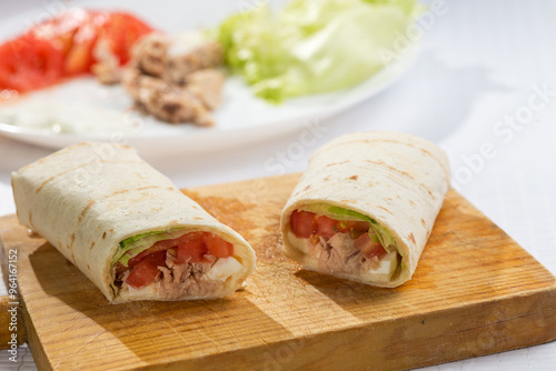 Vegetable fajitas with tomato, lettuce, fresh cheese and tuna, on a wooden board with ingredients in the background.