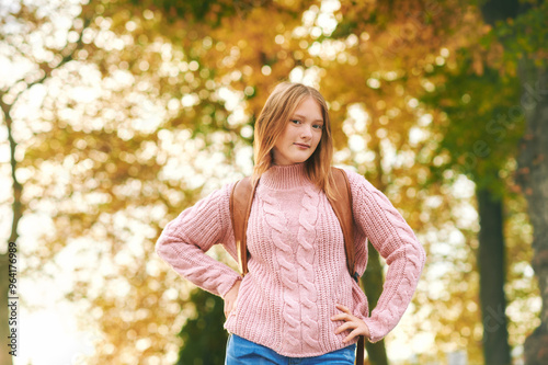 Aurumn portrait of friendly teenager girl posing outdoors with yellow foliage background, wearing backpack