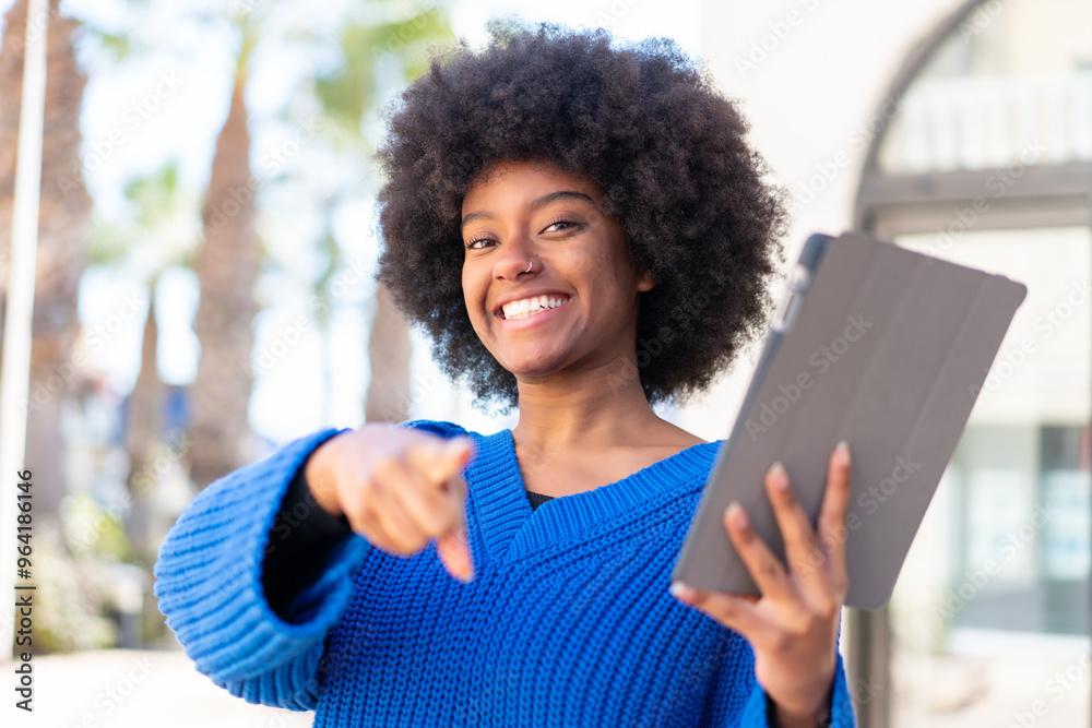 Fototapeta premium African American girl holding a tablet at outdoors points finger at you with a confident expression