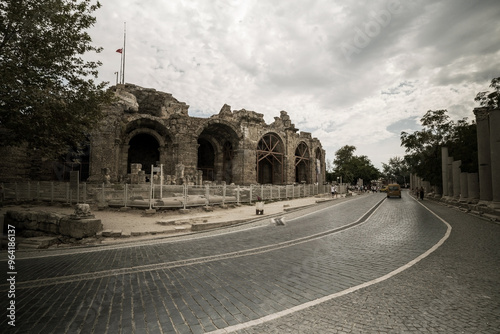 Obraz na płótnie A cobblestone road curves past the ancient amphitheater in Side, Turkey. The amphitheater's weathered stone facade stands tall against a cloudy sky. w salonie