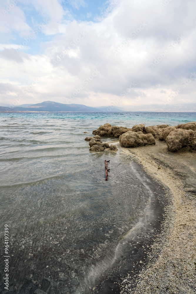 Turquoise waters and white mineral beaches of Lake Salda, Turkey, with a cloudy sky and rocky formations in the background.