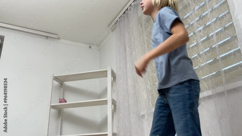 Young boy walking in a room, approaching and moving away from a white shelf, showcasing playful energy and carefree movement Young boy walking in a room, approaching and moving away from a white shelf, showcasing playful energy and carefree movement