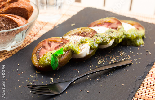 Caprese salad with mozzarella, black tomatoes and pesto on black stone plate photo