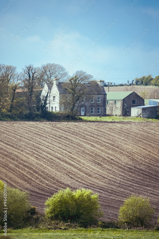 Obraz premium A plowed field stretches out in the foreground, with a house and a barn situated in the background. Trees and bushes line the edge of the field.