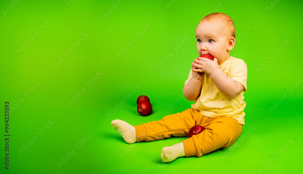 Baby Eating Red Apple. A baby is sitting holding an apple and taking a bite. The child seems to be enjoying the healthy snack while sitting in a relaxed position.