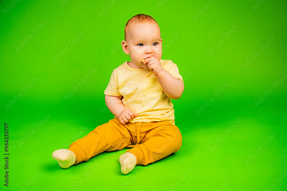 Toddler in Yellow Shirt Enjoys Eating a Piece of Liver on Green Background. A toddler bites into a piece of liver while sitting calmly on a vibrant green backdrop. Toddler in Yellow Shirt Enjoys Eating a Piece of Liver on Green Background. A toddler bites into a piece of liver while sitting calmly on a vibrant green backdrop.