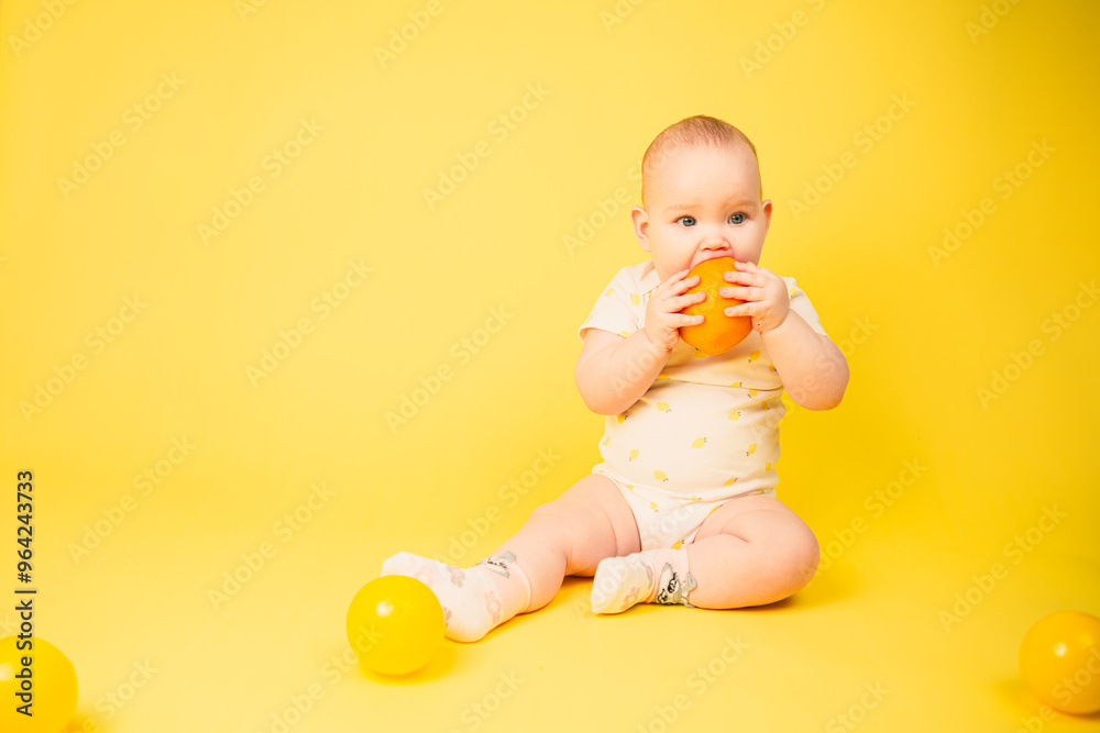 Beautiful baby girl holds orange sitting in studio on yellow background. Beautiful baby girl holds orange sitting in studio on yellow background.