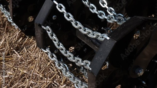 Close-up of a soil tiller with chains for loosening and leveling the ground. Used in farming for pre-planting preparation. Ideal for agricultural and machinery-related content. photo