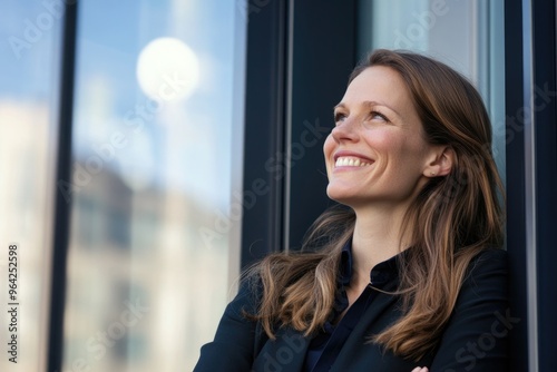 A woman in a business suit is smiling and looking out the window. She is happy and content