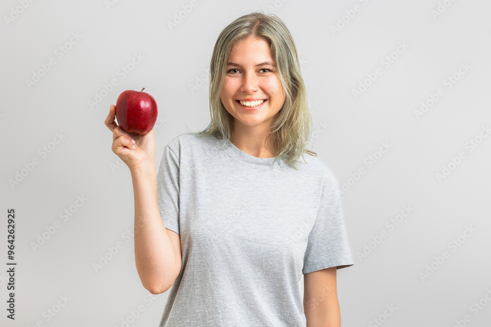 Young beautiful woman wearing gray tee-shirt and holding a red apple. Isolated on gray background Young beautiful woman wearing gray tee-shirt and holding a red apple. Isolated on gray background