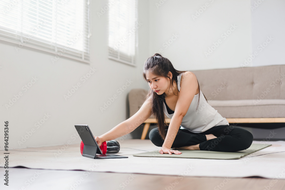 Obraz premium Young Asian woman at home doing exercise in front of open laptop, repeating instructions by professional online fitness trainer.