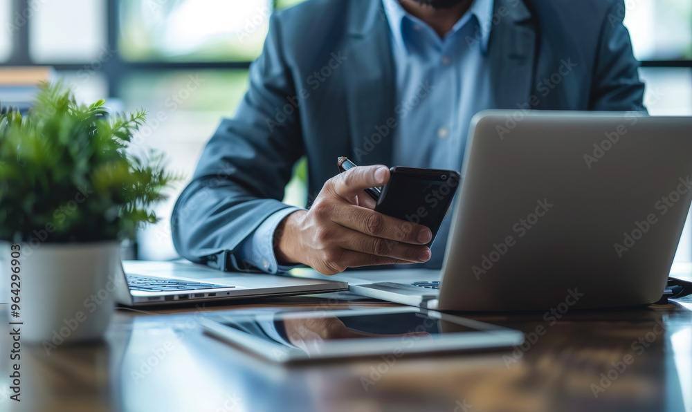 Middle-aged professional man using smartphone, laptop, tablet on desk - busy office work, business meeting preparation Middle-aged professional man using smartphone, laptop, tablet on desk - busy office work, business meeting preparation