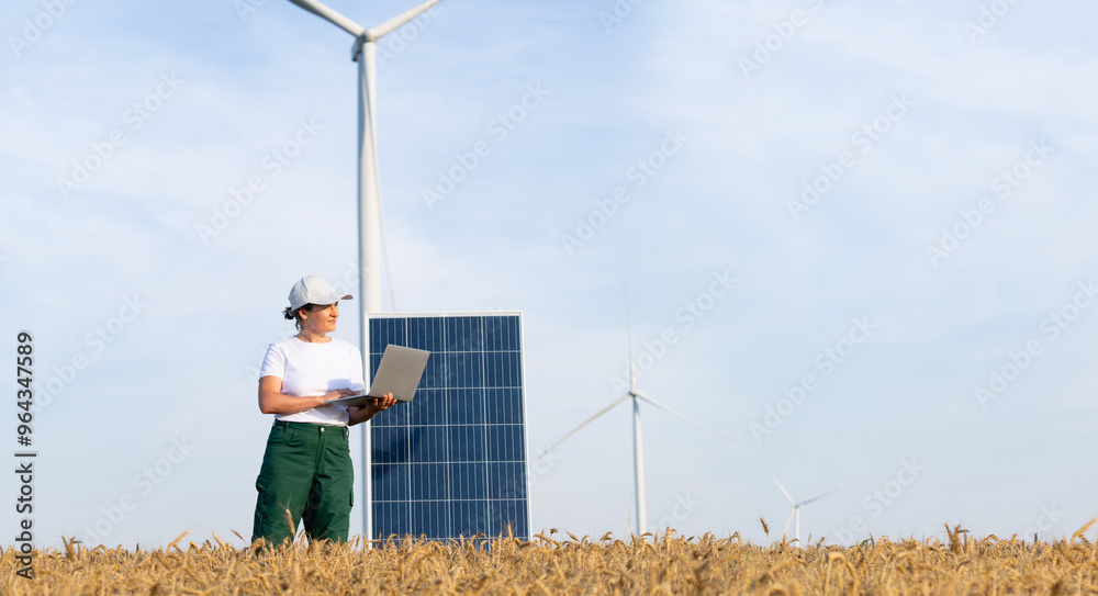 custom made wallpaper toronto digitalWoman farmer wearing white cap and t-shirt with laptop stands next to solar panel. Wind turbines in the background.