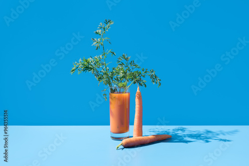 Jugo de zanahoria adornado con hojas verdes en un vaso transparente sobre fondo azul	 photo