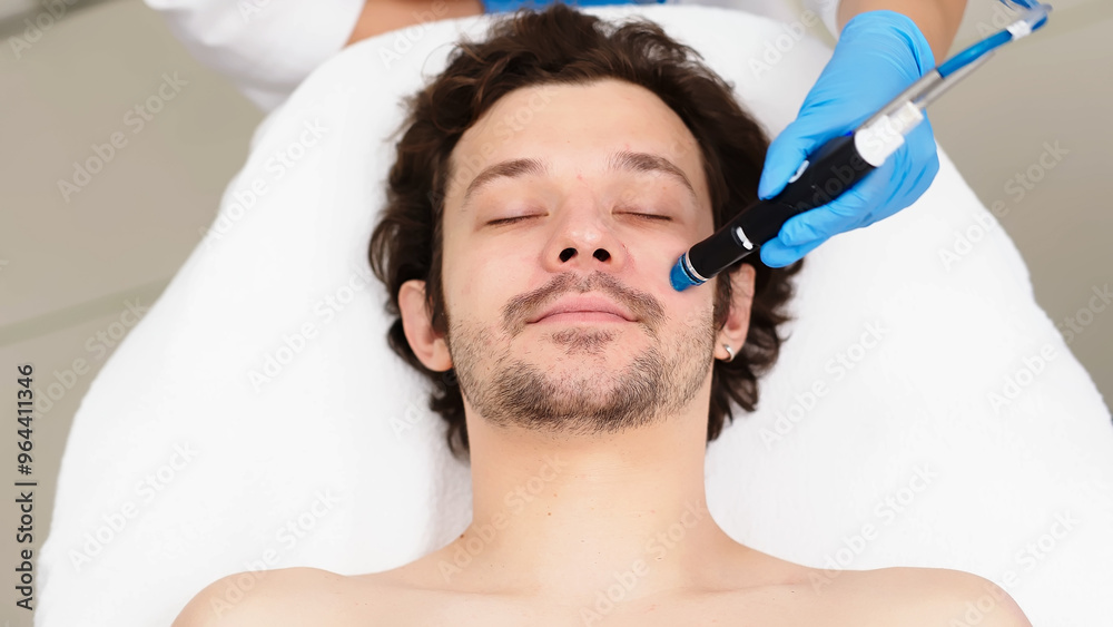 Facial skin care. A professional female cosmetologist performs a hydraulic procedure on a man in a cosmetology clinic. Vacuum cleaner Hydra. Rejuvenation and hydration