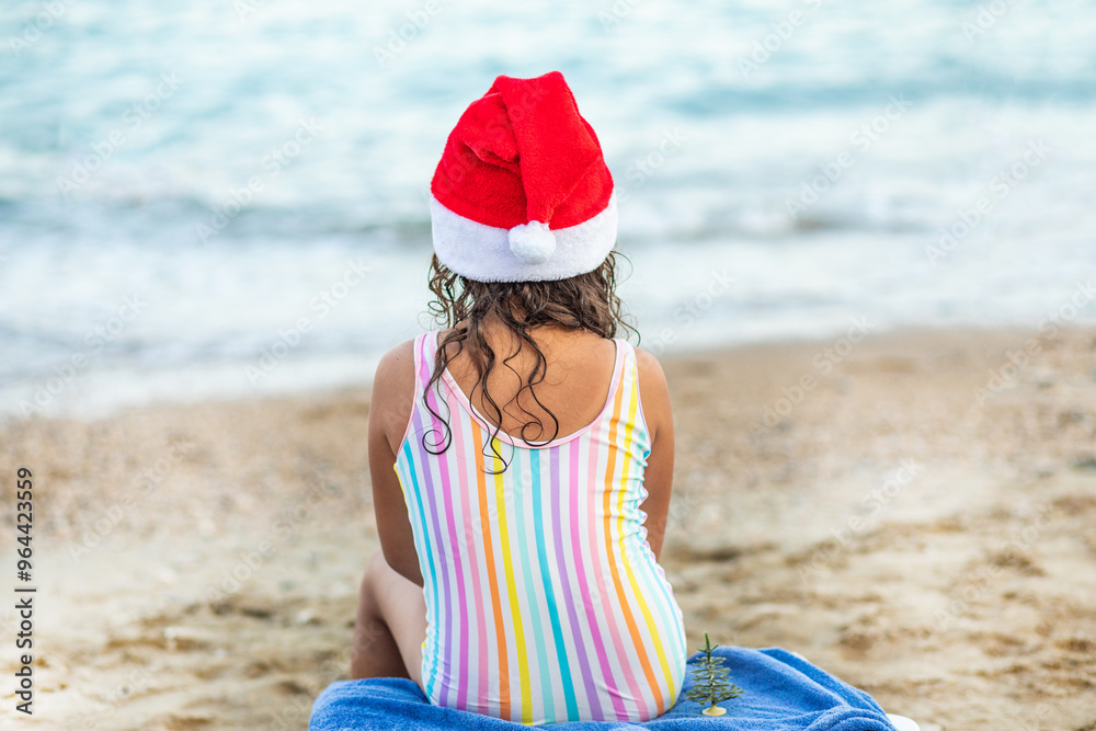 Girl from behind sitting on chaise lounge in Santa hat. Christmas tropical vacation on the beach. Girl from behind sitting on chaise lounge in Santa hat. Christmas tropical vacation on the beach.