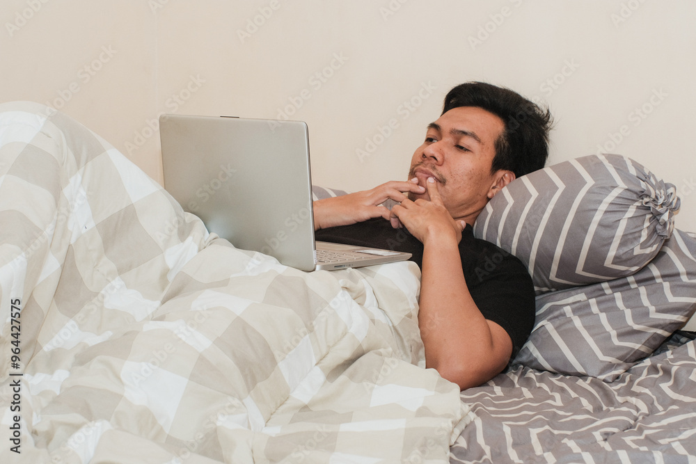 A Southeast Asian man in bedroom and laptop for work from home, serious or thingking in bed for freelance idea. Technology, entrepreneur and remote worker for online job. A Southeast Asian man in bedroom and laptop for work from home, serious or thingking in bed for freelance idea. Technology, entrepreneur and remote worker for online job.