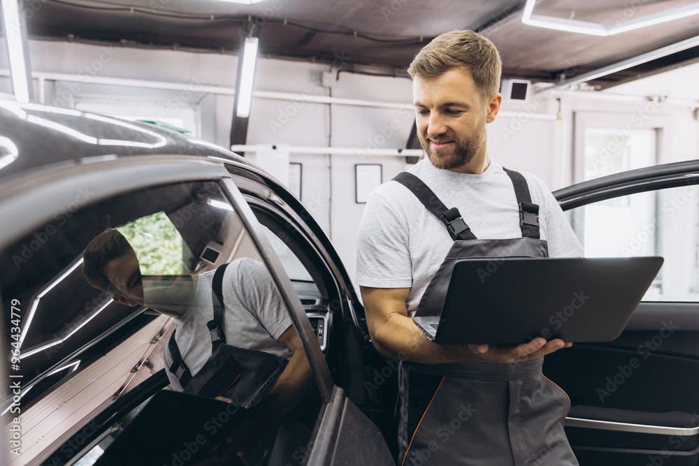 Young professional technician car mechanic man in grey overalls t-shirt use hold laptop pc computer make diagnostics fix problem in vehicle repair shop workshop indoor. Young professional technician car mechanic man in grey overalls t-shirt use hold laptop pc computer make diagnostics fix problem in vehicle repair shop workshop indoor.