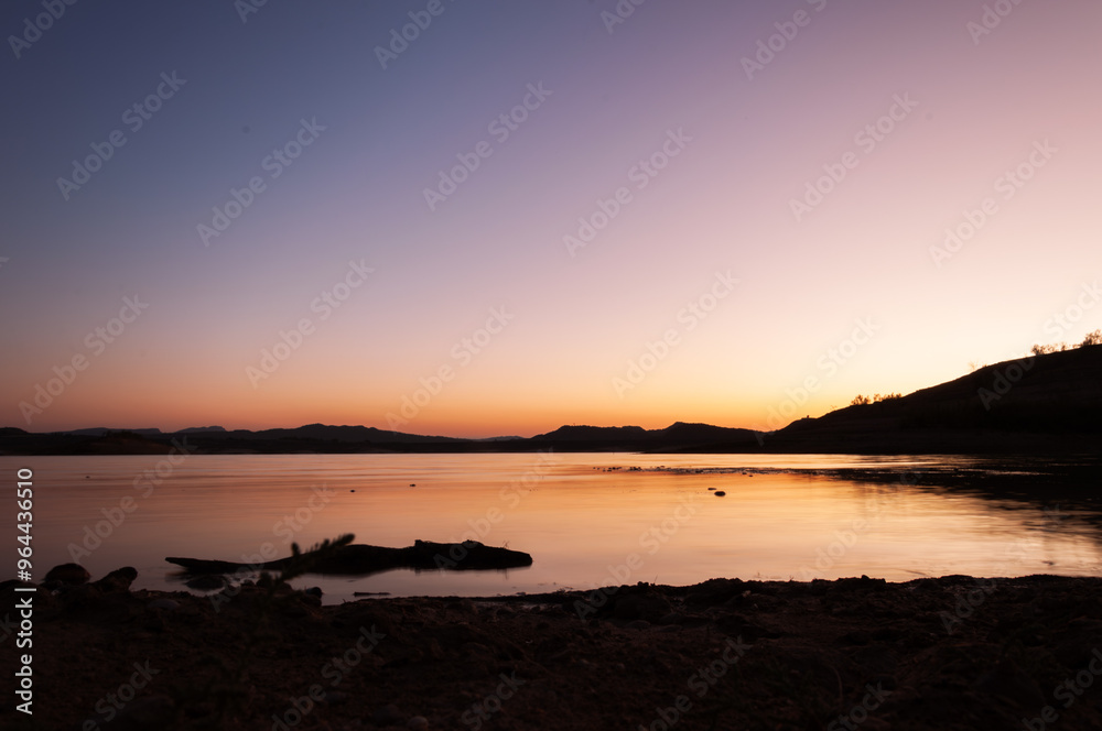 Fototapeta premium Vibrant sunset colors create tranquil atmosphere over lake, reflecting in calm water