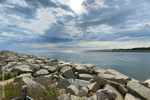 View of Cape Cod Canal MA. Rocky shoreline looking over canal on a cloudy day with sun peaking through clouds. photo