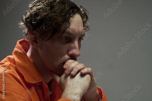 Canvas Print Contemplative man wearing orange jumpsuit resting chin on hands, pensive express