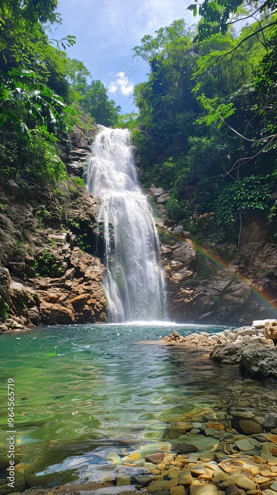 Fototapeta premium A majestic waterfall cascades through a lush forest, with a rainbow forming in the mist.