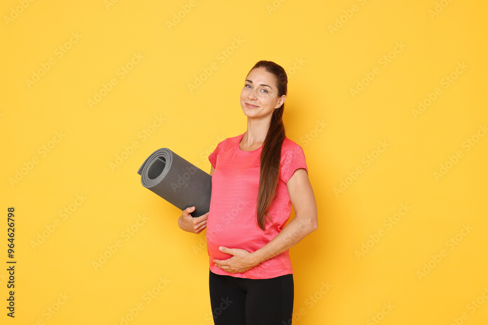 Beautiful pregnant woman with exercise mat on yellow background