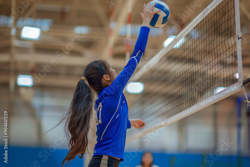 Girl in a blue shirt is about to hit a volleyball. The girl is wearing a ponytail and is reaching for the ball photo