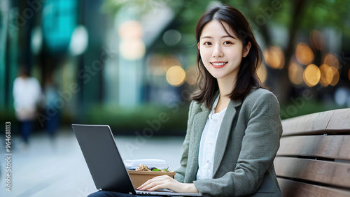 A young and beautiful Korean woman in her late twenties is sitting on a bench outside with a laptop, smiling at the camera. She has long hair and dress in business attire. 