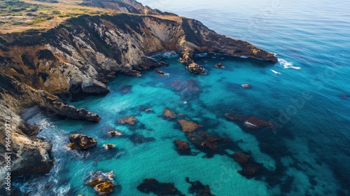 Aerial view of a rugged coastline with crystal-clear blue waters and dramatic rock formations jutting out of the sea
