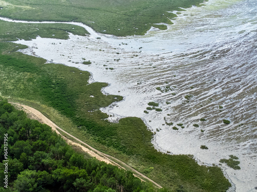 Vue aérienne de la baie à marée basse. L'océan retiré laisse apparaitre le réseau de chemins laissé dans le sable de la baie. Au premier plan une dune avec des arbres et de la pelouse. photo