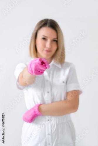 A female doctor in a white uniform and pink gloves points her finger at the camera.