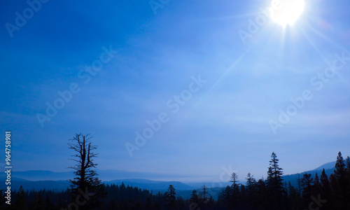 View of a misty valley with sun in upper right corner of the sky. 