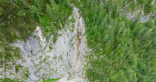 Aerial dolly out shot with a drone of the Martuljek upper waterfall called zgornji slap near a cliff on a overcast summer day, surrounded by a green forest in the julian Alps