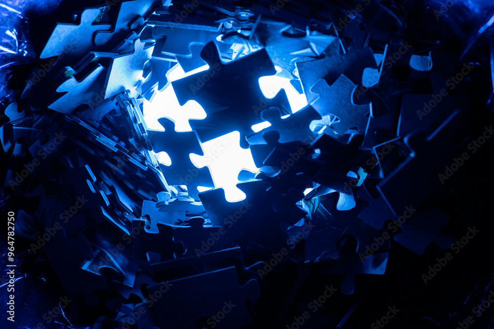 Pile of dark puzzle pieces illuminated by bright blue light