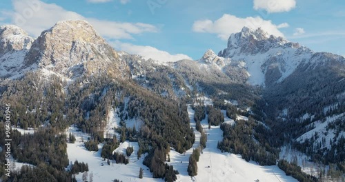 Panoramic pan shot with a drone showing the pragser ski resort in the foreground and two mountain peaks named (left to right )Sarlkofel and Dürrenstein in the alps, sunny winter day