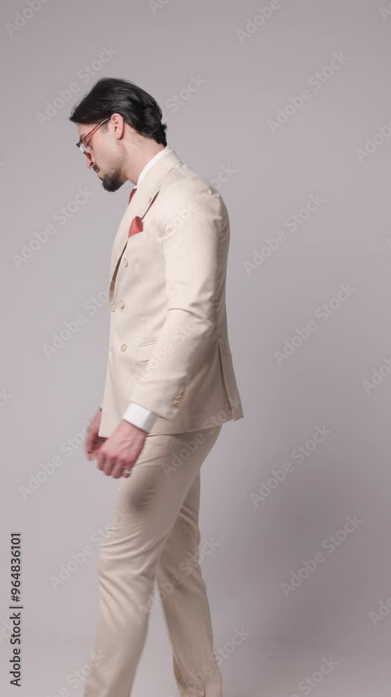 cool fashion man in beige suit rubbing palms, turning around, holding hand in pocket, adjusting suit and being arrogant on grey background cool fashion man in beige suit rubbing palms, turning around, holding hand in pocket, adjusting suit and being arrogant on grey background