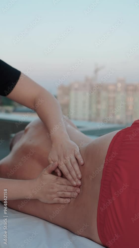 Master massage therapist on the roof of a house in the city gives a massage to a beautiful young man with a tattoo, close-up hands lubricating skin and body with oil. Medicine and procedure Master massage therapist on the roof of a house in the city gives a massage to a beautiful young man with a tattoo, close-up hands lubricating skin and body with oil. Medicine and procedure