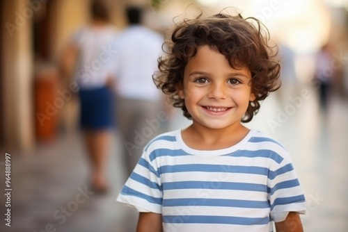 A young boy with curly hair is smiling and wearing a striped shirt