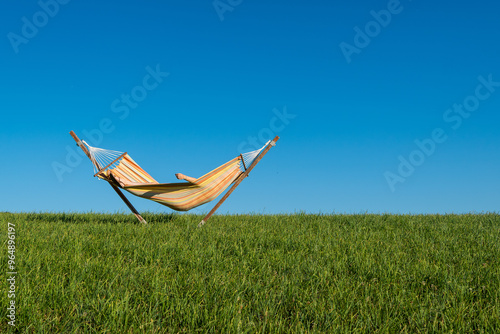 un hamac duquel dépasse un bras , au milieu d'un pré vert, sous un grand ciel bleu