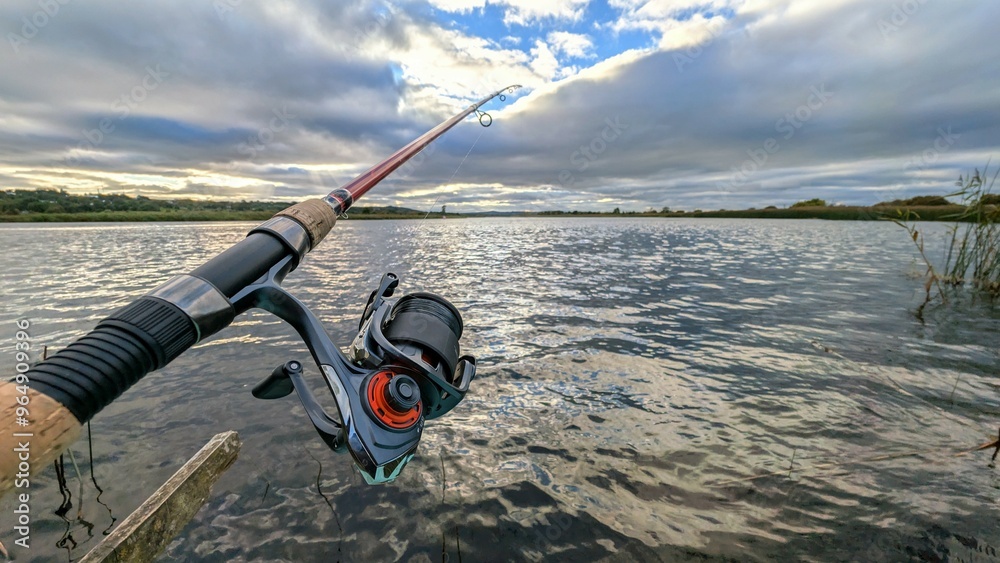 Hand holding fishing rod and reel, fishing at Corrib river at Galway, Ireland, spinning, angling, catch and release, sport and leisure, nature background