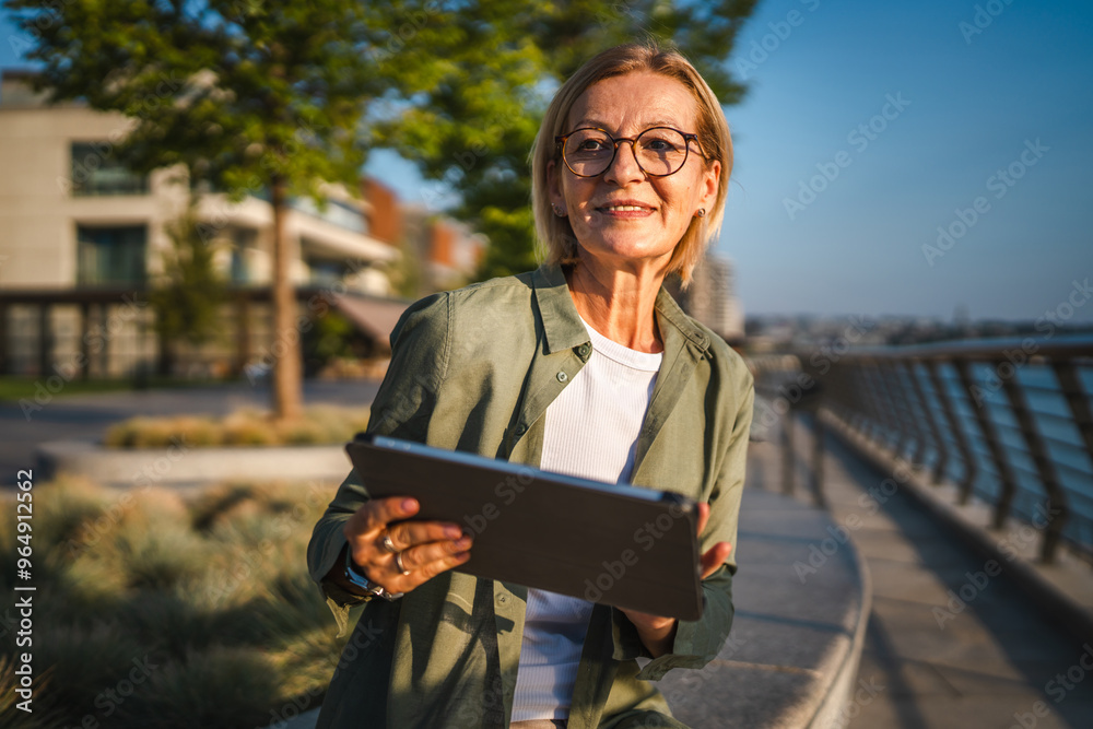 Fototapeta premium mature woman sit near river and use digital tablet