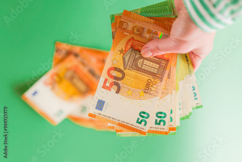 Money fan made of euro bills.Cash payments in the European Union.Benefits, subsidies, wages and pensions in Europe.Hand in striped blouse holding euro bills fan on green background.