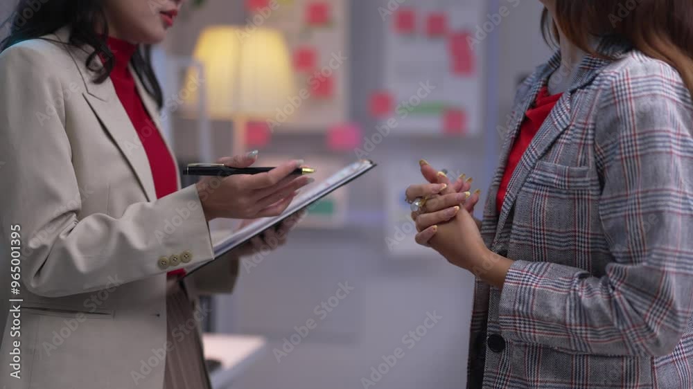 Two businesswomen engage in a discussion, with one taking notes on a clipboard. Their interaction highlights collaboration and communication in a professional office setting Two businesswomen engage in a discussion, with one taking notes on a clipboard. Their interaction highlights collaboration and communication in a professional office setting