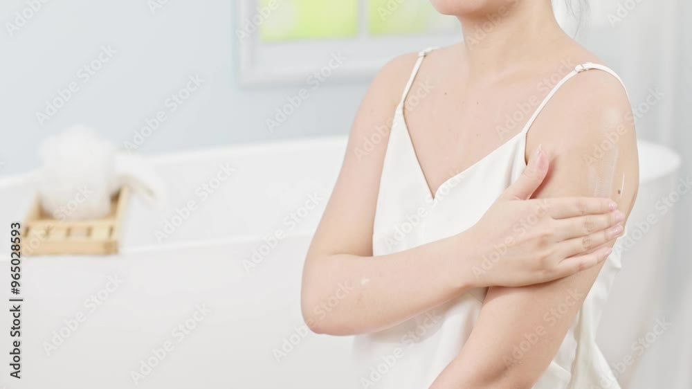 In the bathroom space with a large bathtub and window, the girl gently applied smooth white cream to her arm. Scene of applying skin cream at home. Professional promotional videos In the bathroom space with a large bathtub and window, the girl gently applied smooth white cream to her arm. Scene of applying skin cream at home. Professional promotional videos