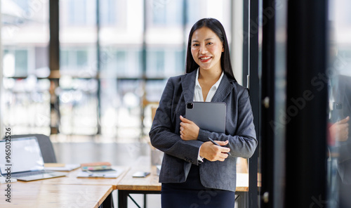 Modern business asian woman in formalwear using digital tablet while standing near wooden desk in an office interior in the office. business people concept. photo